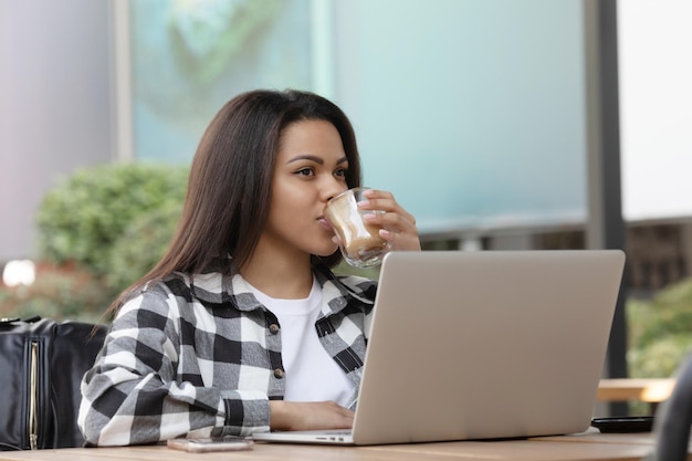 Focused young African woman sitting alone at a counter in a cafe working on a laptop