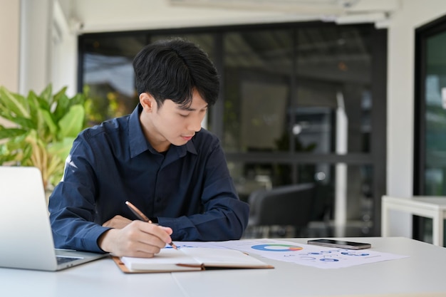Сосредоточенный молодой азиатский финансовый аналитик или бухгалтер, работающий над финансовым отчетом