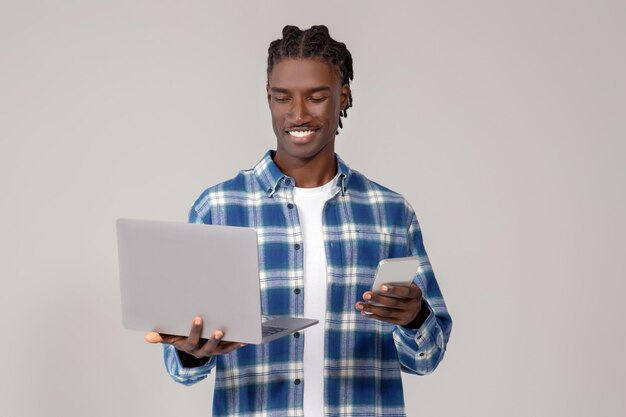 Focused young black man using laptop and holding smartphone