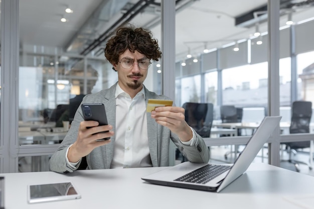 Focused young businessman with curly hair multitasking in a modern office working on a laptop while