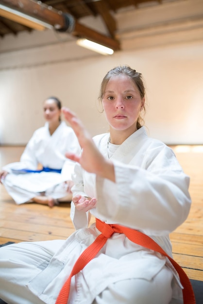 Focused young Caucasian karate girl sitting in studio. Sporty karateka ready for class in academy. Sports, martial arts, healthy lifestyle concept