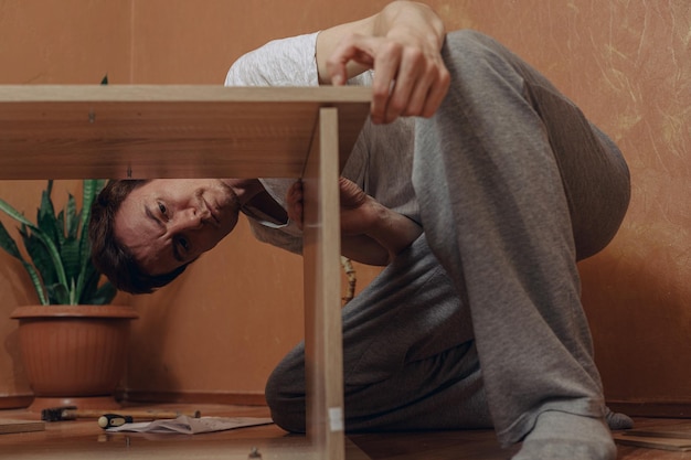 Focused young man assembling furniture and examining new wooden table at home