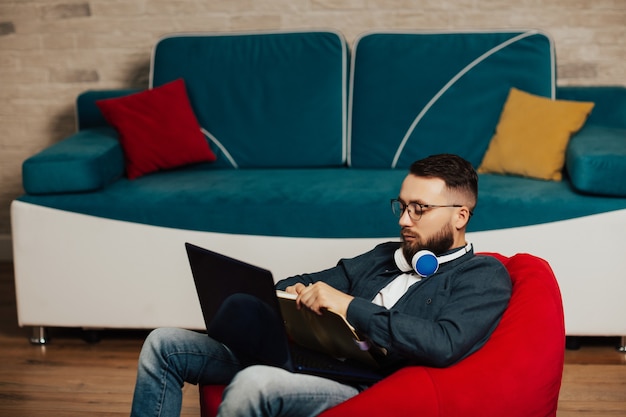 Focused young man wear headphones study online, watching webinar on laptop or education course and make notes.