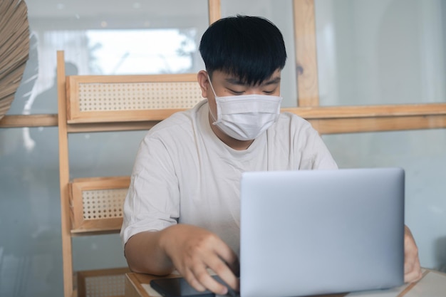 Focused young man wearing a medical mask using laptop typing on keyboard writing email