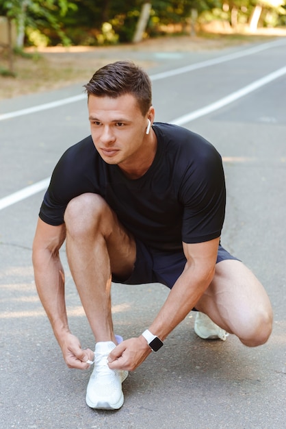 Focused young sportsman in earphones tying his shoelace