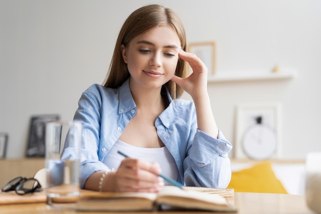 Сосредоточенная молодая женщина пишет письмо на столе в домашнем офисе Сосредоточенная деловая женщина делает заметки в блокноте за столом в гостиной