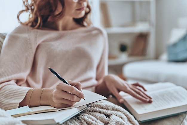 Photo focusing on education. close up of young women writing something down while sitting on the sofa at home