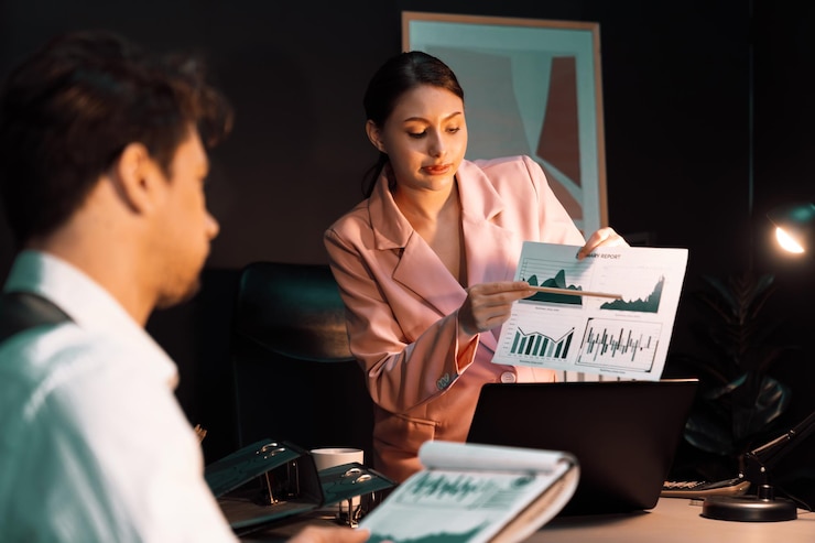Photo focusing on woman presenting graph while man holding paper to sign postulate