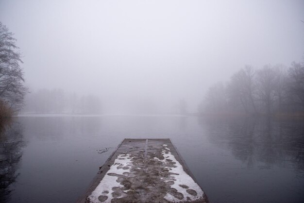 Photo fog on the lake a small bridge on which there are traces of people in the snow