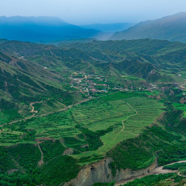 Foggy highland valley with vliiage and fields between mountain\
peaks