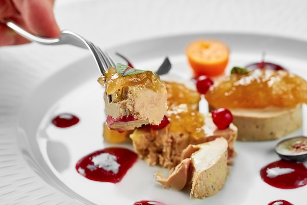 Foie gras with apple confit and berry sauce in a white plate on a white background Closeup selective focus