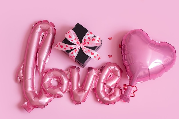 Foil balloon in love and heart shape with gift box on pink background Valentines Day concept