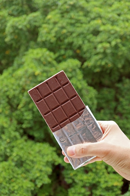 背景にぼやけた緑の葉と手にチョコレートバーのホイルパック