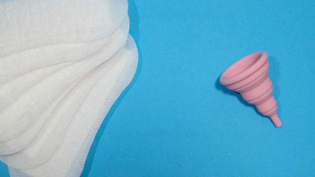 Foldable pink menstrual cup and disposable pads on a blue background. Sustainable menstruation