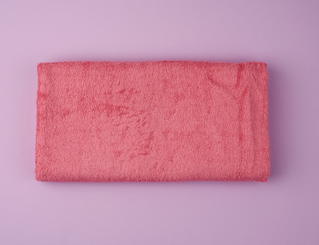 Asciugamano piegato di rosa di spugna del bagno su un fondo bianco