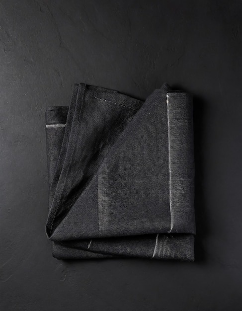 Folded black linen linen kitchen towel on a black background top view