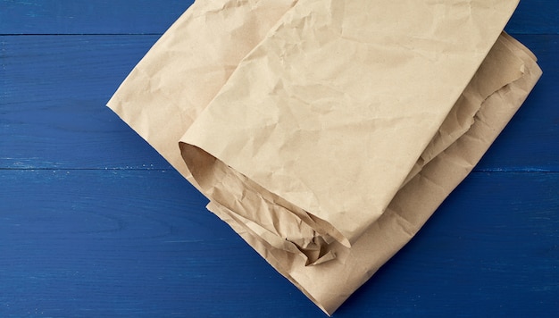 Folded brown crumpled kraft paper sheet on blue wooden background