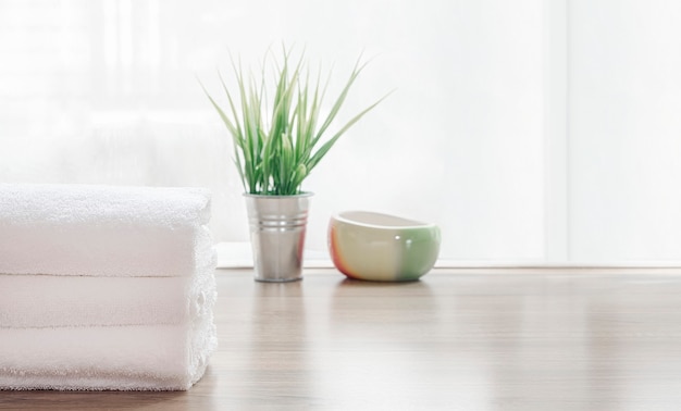 Folded clean white towels and houseplant on wooden table.