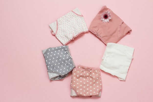 Folded cotton panties of different color with flower on pink background. Woman underwear set. Top view.