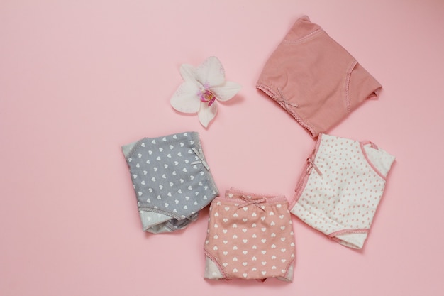 Folded cotton panties of different color with orchid bud on pink background. Woman underwear set. Top view.