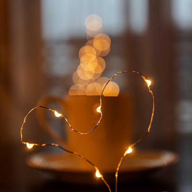 Folded from a garland heart on the  of a blurred cup of coffee or tea, a steam from garland blurred bokeh. Festive mood. Blurred. Defocused.