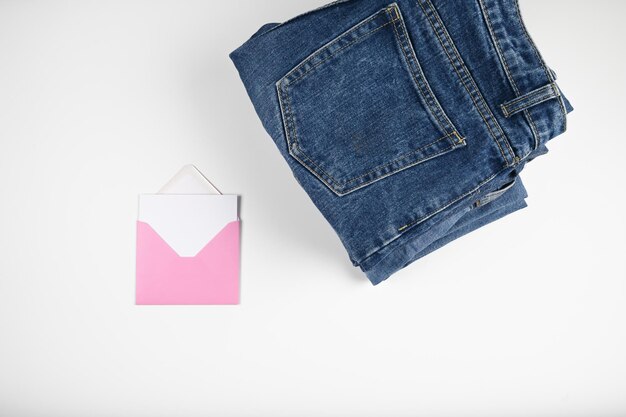 Folded jeans and a pink envelope with a blank card isolated on white Collection of jeans Sales or shopping mock up High quality photo