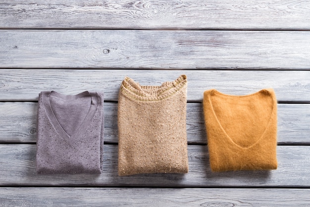 Folded sweaters of different color. Casual pullovers with v-neck. Warm garments on gray shelf. Quality autumn clothes for girls.