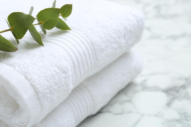 folded terry towels and eucalyptus branch on white marble table closeup