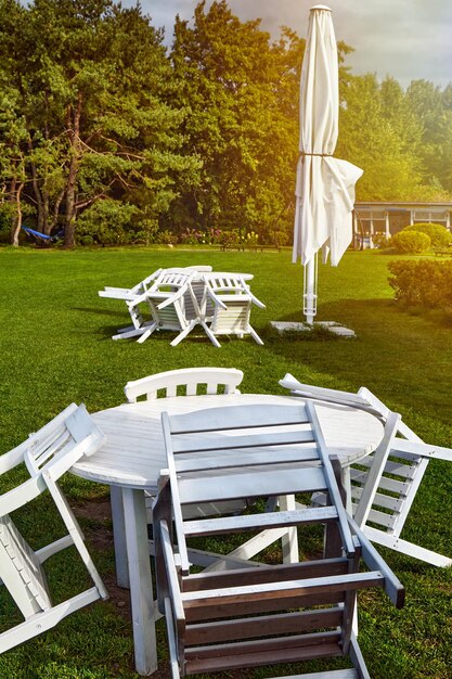 Folded umbrella and street cafe chairs on the morning sunny lawn