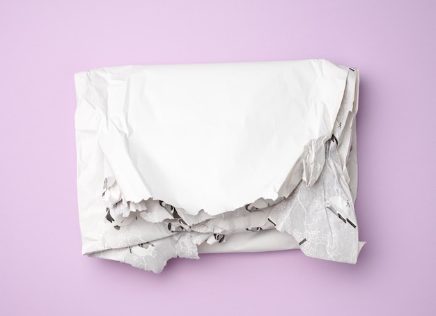Folded wrapping crumpled white paper on purple background top view