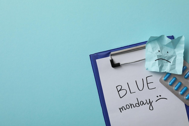 Folder with paper with the text Blue Monday pills and note with sad emoji on blue background space for text