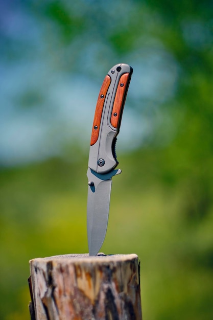 Photo folding knife is stuck in wooden stump against background foresttool for outdoor recreation