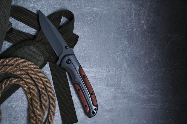 Folding knife for survival a rope and a khaki backpack strap on a gray concrete background