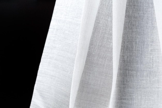 Folds of white satin cotton transparent textile on a black background