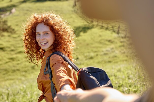 Follow me attractive curly woman takes mans hand leads in the forest to hike travel smiling happily ...