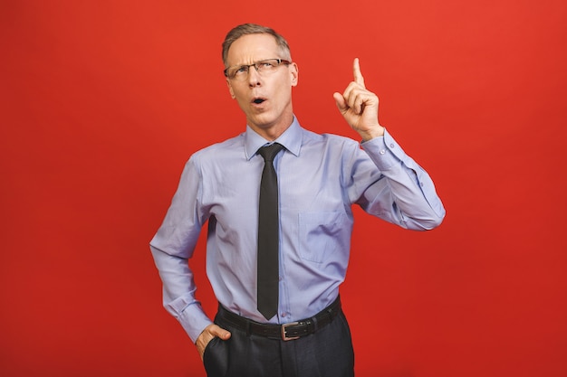 Follow me! Look here! Close up portrait of cheerful satisfied pleased qualified experienced joyful aged businessman pointing on empty blank place isolated on red wall.