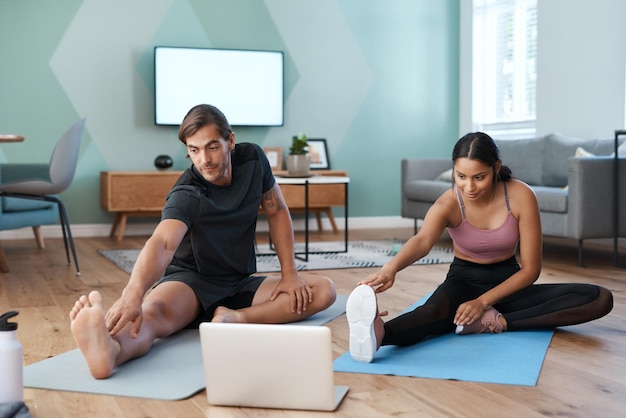 A seguito di una lezione di fitness online foto a tutta lunghezza di una giovane coppia atletica che si allunga davanti a un laptop durante l'allenamento a casa