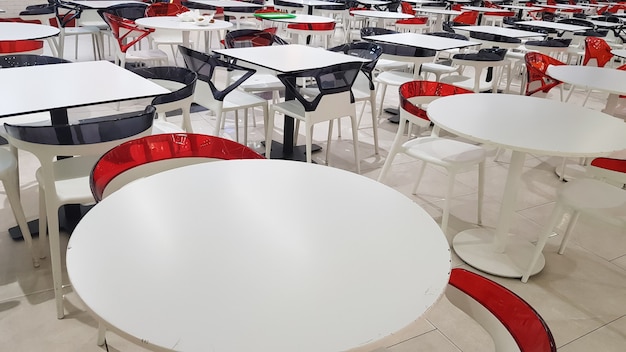 사람들이 없는 쇼핑몰에 플라스틱 흰색과 빨간색 테이블과 의자가 있는 음식 공간.
