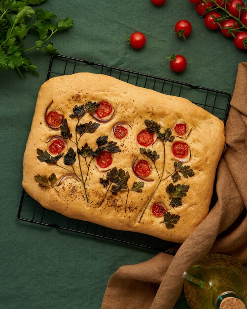 Food art focaccia flatbread with tomatoes on dark green linen textile tablecloth top view