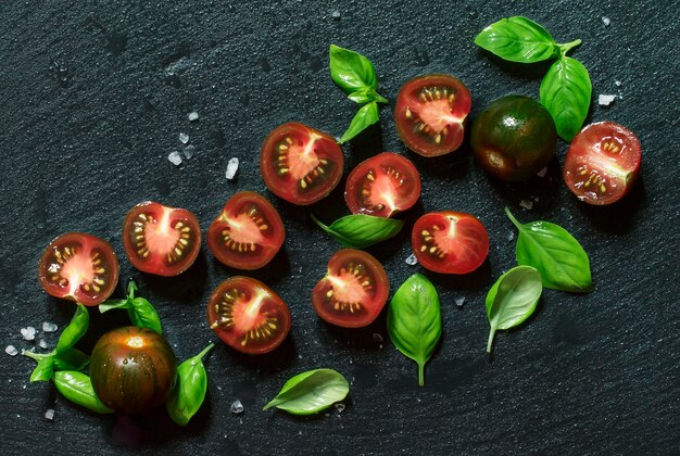 Food background black and red cherry tomatoes and green basil on a wet stone background top view