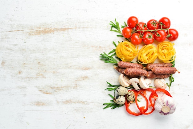 Food background Dry pasta tomatoes spices and vegetables on a white wooden background Top view