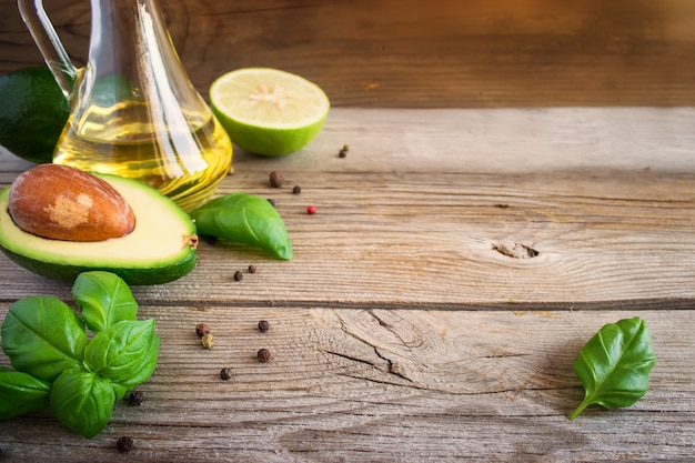 Food background with avocado, lime, olive oil and basil on old weathered boards.