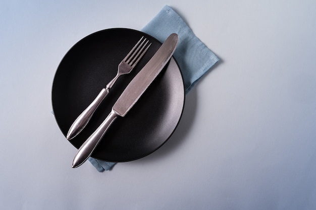 Food background with empty black plate, cutlery and napkin on blue