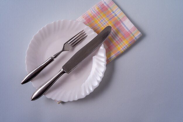 Food background with empty white plate, cutlery and napkin on blue