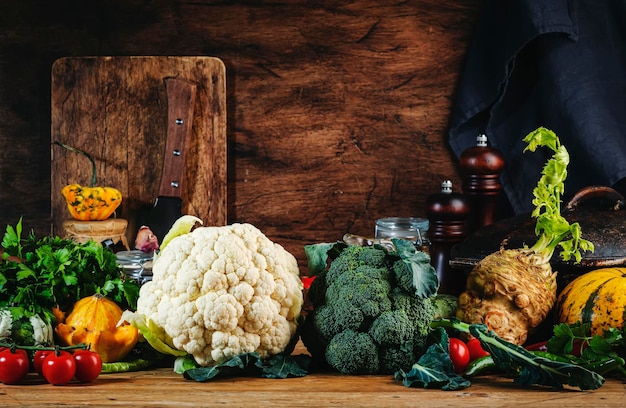 Foto sfondo di cibo con verdure di fattoria cavolfiore radice di broccoli sedano zucca pomodori erbe e spezie sul tavolo da cucina in legno rustico con padella in ghisa tagliere per spezie