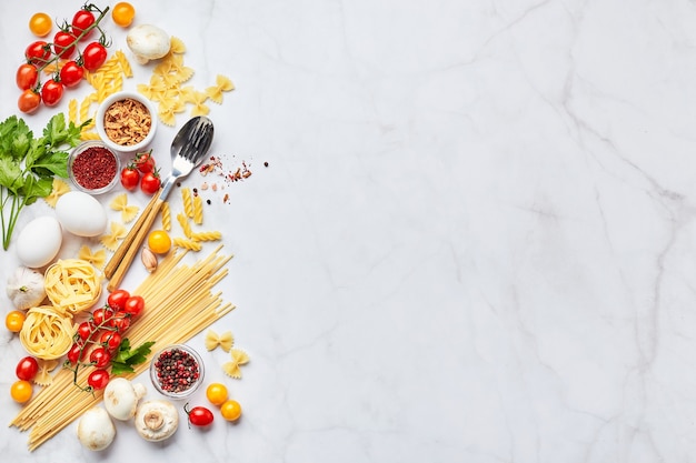 Food background with place for text, with different kinds of pasta, tomatoes, herbs, mushrooms, eggs, seasonings scattered on light marble background, top view. Italian cuisine concept