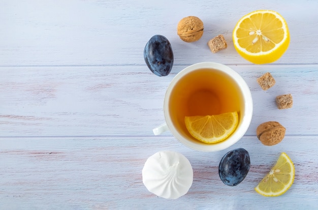 Food background with white porcelain cup of tea, lemon, plums, nectarines, walnuts and marshmallow