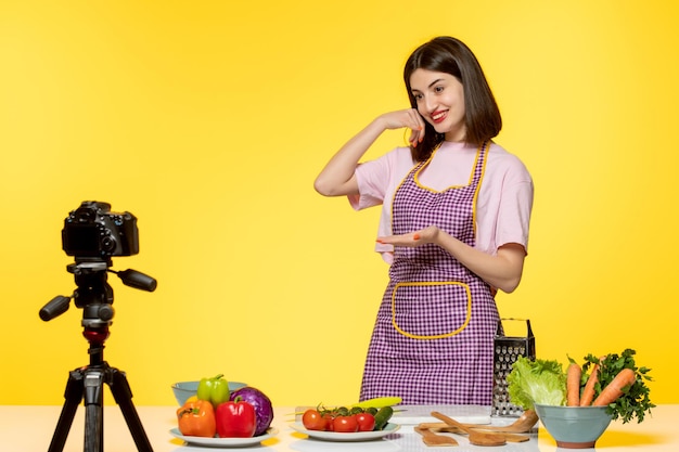 Food blogger ragazza carina in grembiule rosa con registrazione video sorridente con verdure