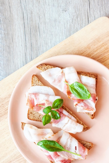 Foto colazione alimentare un piatto con panini pane di segale con fetta di pancetta e foglia di basilico