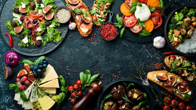 Food cheese figs mushrooms meat and vegetables European and Asian cuisine Healthy food on a black stone background Top view